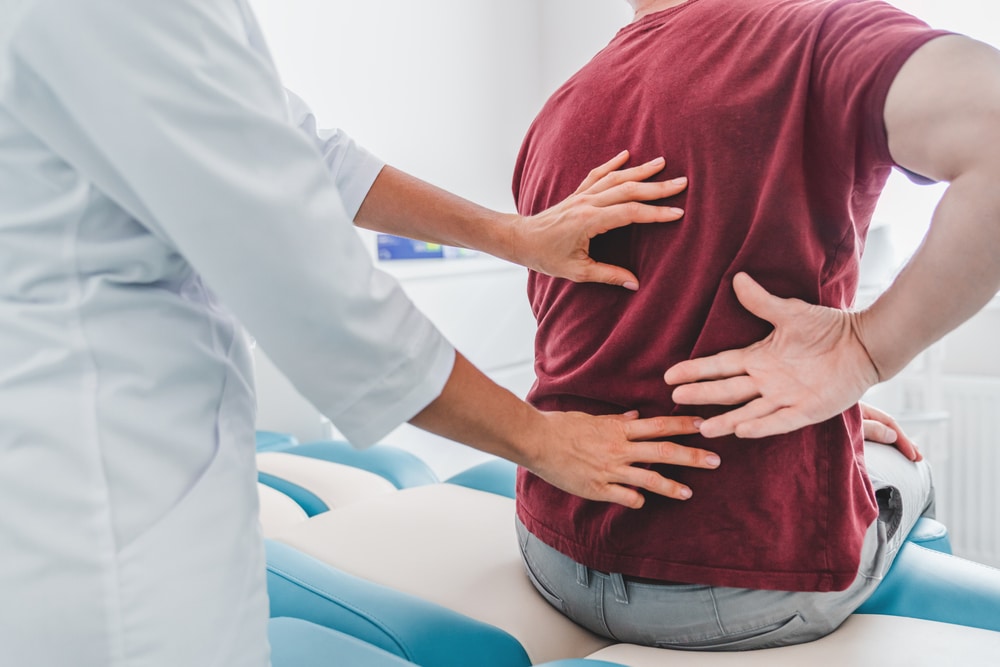 CroppedCloseUpOfFemaleOrthopedistExaminingPatientsBackIn